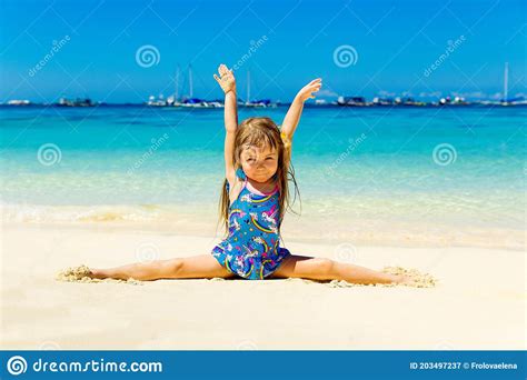 Smiling Little Girl Doing Gymnastics Splits On A Sandy Tropical Beach