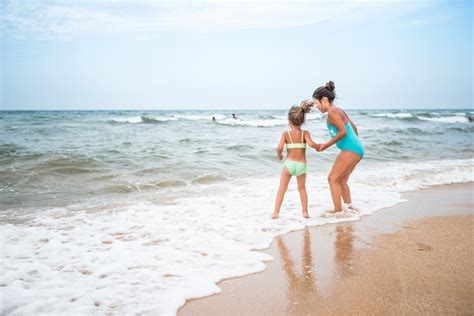 Две очаровательные девочки в купальниках танцуют на песчаном пляже у моря на фоне голубого неба