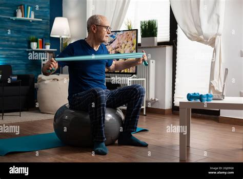 Retiree Senior Man Sitting On Swiss Ball In Living Room Doing Healthcare Fitness Exercises