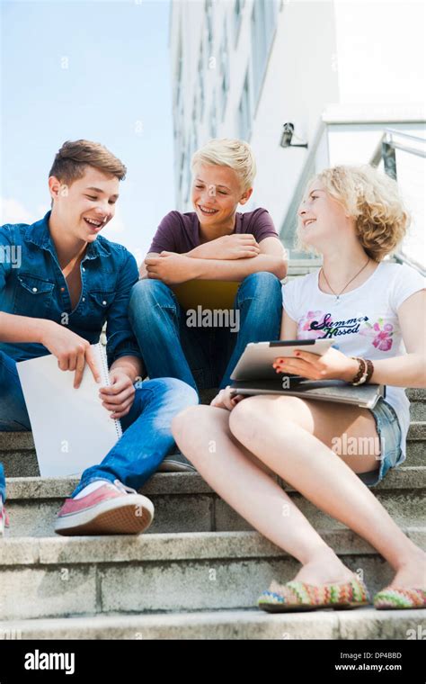 Teenagers Sitting On Stairs Outdoors Talking And Looking At Tablet
