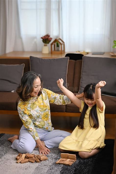 Happy Mature Grandmother Having Fun Playing With Cute Little Preschooler Granddaughter In Living