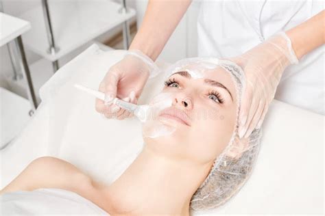 Cosmetologist Applies Cream Mask On Woman Face For Rejuvenation Face Skin Procedure In Beauty