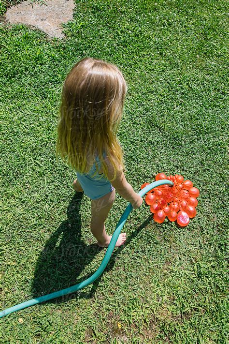Summer Lifestyle Young Girl Inflating Water Balloons In Backyard By