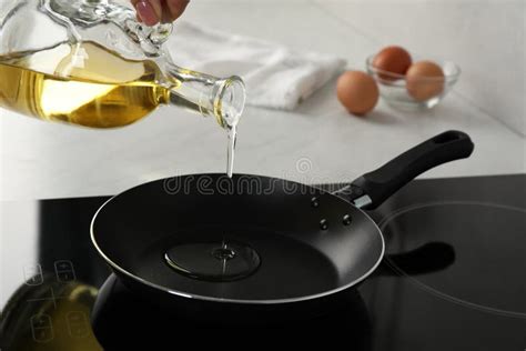 Woman Pouring Cooking Oil From Jug Into Frying Pan On Stove Closeup