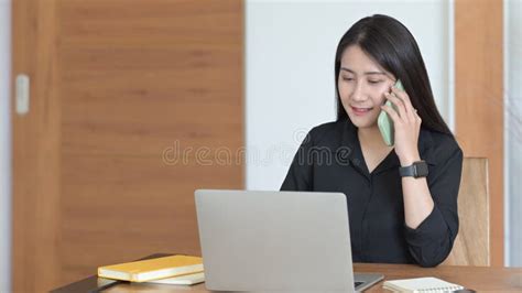 Female Entrepreneur Working On Laptop Computer And Having Conversation On Mobile Phone Stock