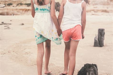 Image Of Behind View Of Two Girls Walking Along The Beach Holding Hands