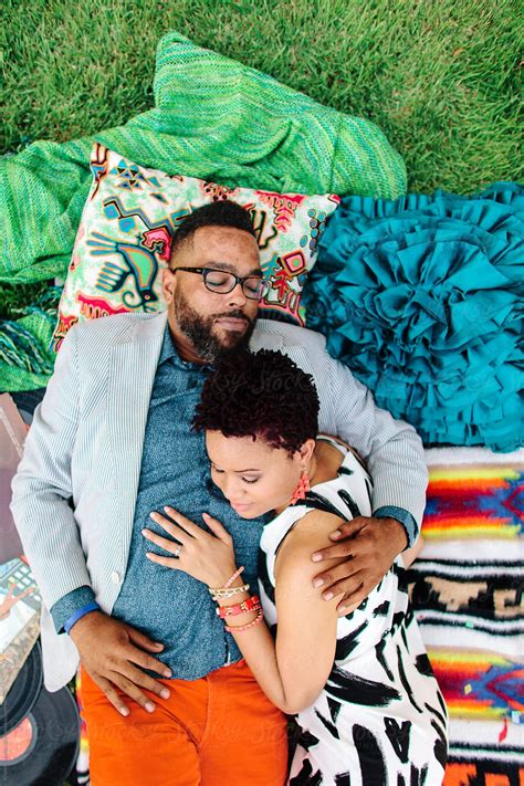 A Hipster African American Couple Laying On Blankets In The Park Embracing One Another By