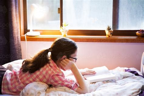 Image Of Teen Person Lying On Her Bed Reading A Fiction Book With Lamp