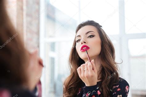 Seductive Woman Applying Red Lipstick To Lips Looking In Mirror ⬇ Stock