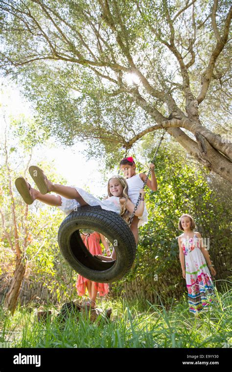 Low Angle View Of Four Girls Playing On Tree Tire Swing In Garden Stock Photo Alamy