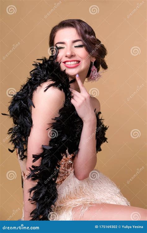 beautiful brunette woman in boa from ostrich feathers is posing and smiling on beige background