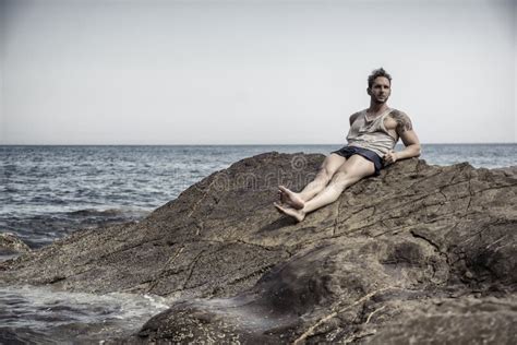 Handsome Muscular Man On The Beach Sitting On Rocks Stock Photo Image