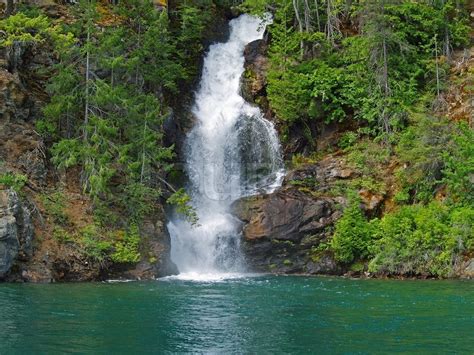 Beautiful Mountain Waterfall Flowing Into A Green Lake Stock Photo