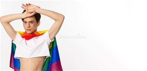 beautiful gay man with glitter on face wearing crop top and rainbow lgbt flag posing against