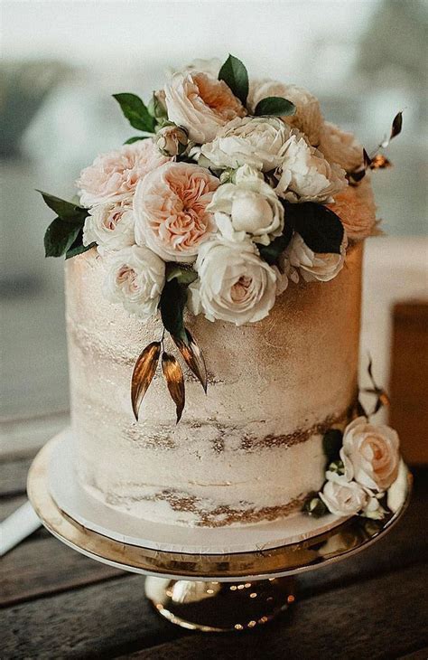 A White And Gold Wedding Cake With Pink Flowers On The Top Is Sitting