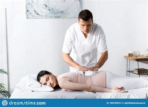 Healer Standing Near Woman Lying On Massage Table With Closed Eyes And Holding Hands Above Her