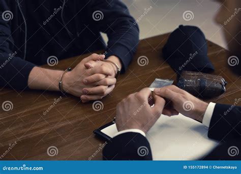 Police Officer Interrogating Criminal in Handcuffs at Desk Stock Photo