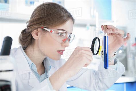 Young Female Scientist Looking At Chemical Sample In Test Tube With