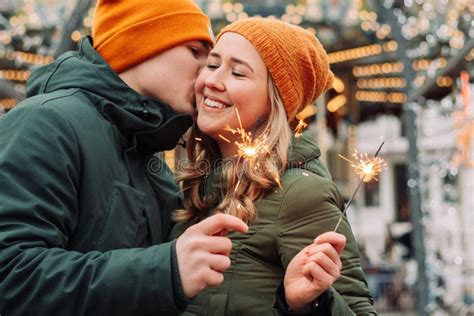 Young Attractive Couple Hug And Kiss Outdoors With The Sparklers In Their Hands Celebrating New