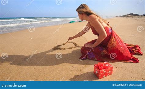 woman in red dress sits draws heart on sand of wet beach stock footage video of sand