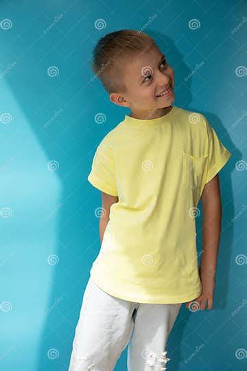 A 6 7 Year Old Boy In A Yellow T Shirt On A Blue Background Looks Up