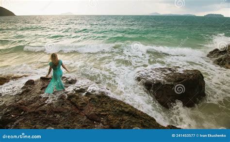 woman walks on rock of sea reef stone stormy cloudy ocean blue swimsuit dress tunic concept