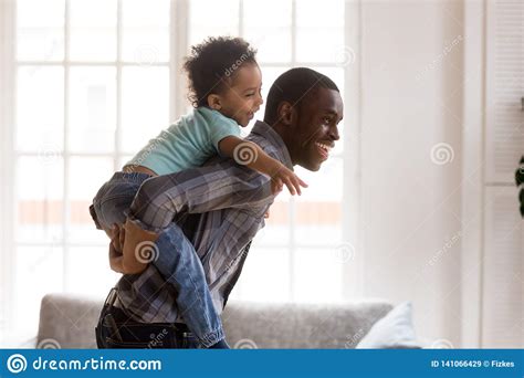 Happy Little Kid Riding Black Dad Having Fun At Home Stock Image