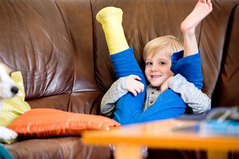 Cute Little Blond Boy With Broken Leg In Cast Sitting On Leather Couch