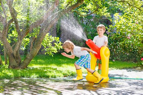 Two Little Kids Playing With Garden Hose And Water In