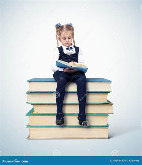 Little Girl Schoolgirl Sitting With A Book On A Stack Of Books