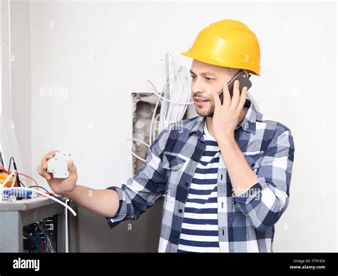 Electrician Talking On Phone Near Distribution Board Indoors Stock