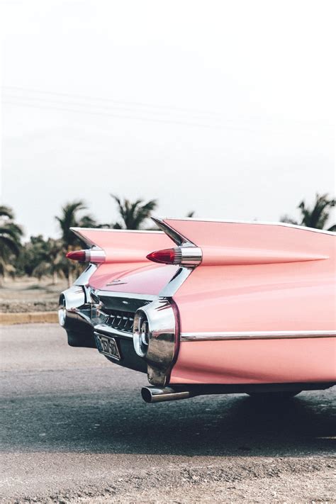 An Old Pink Car Parked On The Side Of The Road With Palm Trees In The