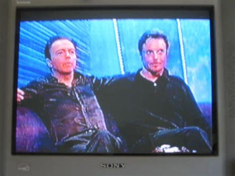 Two Men Sitting Next To Each Other In Front Of A Tv Screen With The Words Sony On It