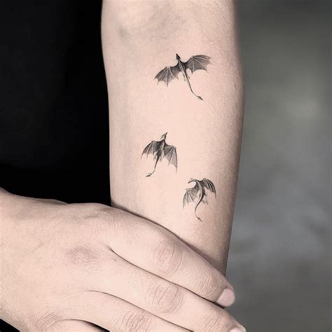 A Womans Arm With Three Small Tattoos On It Including Two Flying Bats