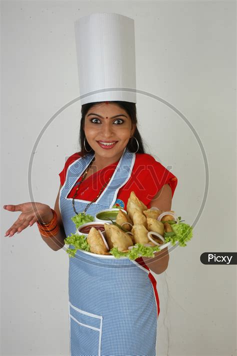 Image Of An Indian Woman Chef In Kitchen Apron And Cap Holding Samosas Plate With An Expression