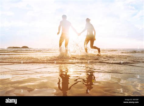 Happy Young Couple Having Fun On The Beach At Sunset Water Splash