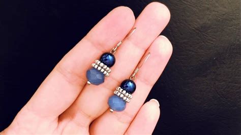 A Pair Of Blue And White Beaded Earrings On Someone S Hand In Front Of