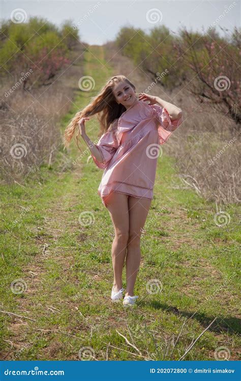 Beautiful Blonde Woman In Pink Dress Walks Through The Flowering Garden