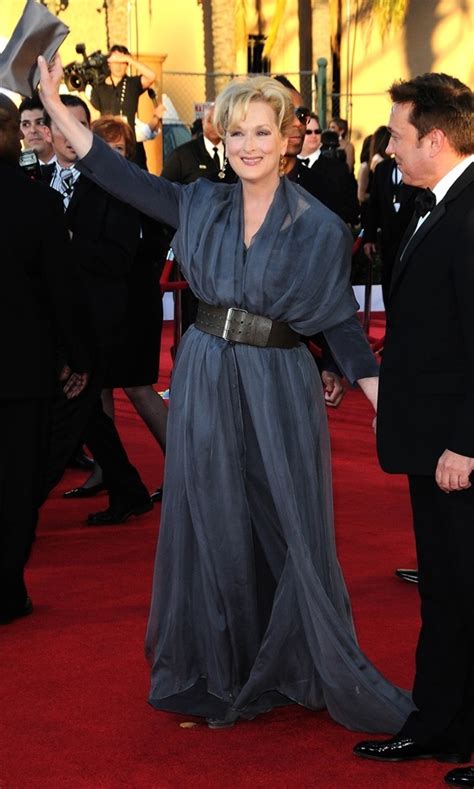 A Woman In A Gray Dress Waves To Someone On The Red Carpet