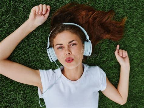 beautiful woman in headphones listening to music lying on the grass green lawn in the park in