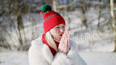 A Blonde Girl In A Red Hat Freezes And Blows On Her Hands In A Cold