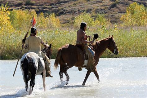Two Native American Indian Men On Horseback Walking Through A River