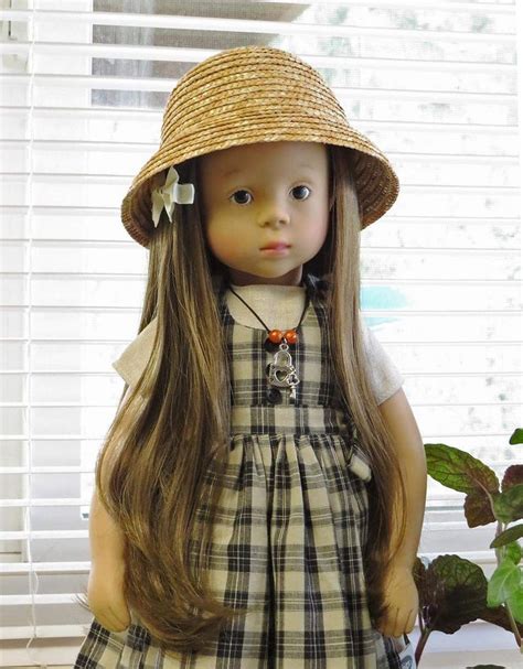 a doll with long hair wearing a dress and hat standing in front of a window