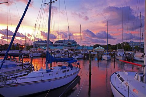 Several Sailboats Docked At A Marina With The Sun Setting In The Sky