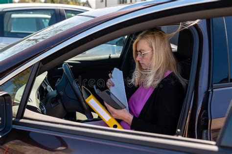 Middle Aged Blonde Business Woman In Glasses In Car Working With