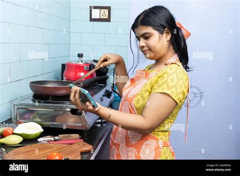 A Pretty Indian Young Woman Wearing Apron Watching Cooking Video In Smart Phone In Domestic