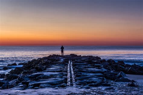 Silhouette Photo Of Person Standing On Rock Facing Sea During Sunset Hd