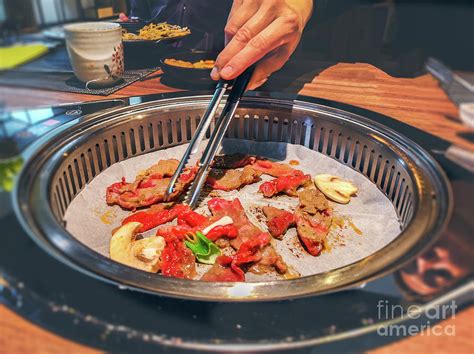female hand cooking korean bulgogi griller beef in a bbq grill on restaurant table photograph by