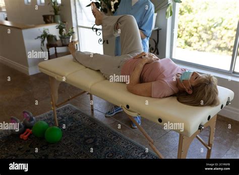 senior caucasian woman at home visited by caucasian female nurse stretching her leg wearing