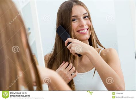 Beautiful Young Woman Brushing Her Long Hair In Front Of Her Mirror